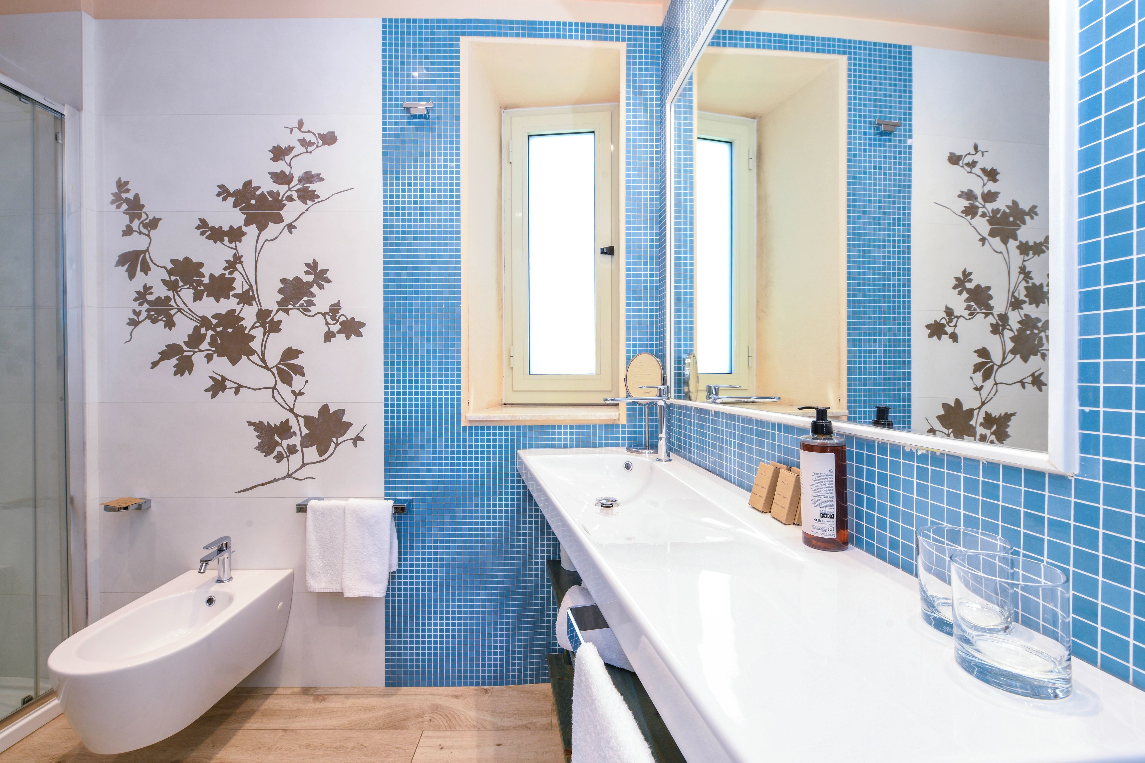 A bathroom with a bidet, a white sink, a mirror, and blue tiles with floral patterns.