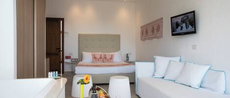 Una habitación de hotel moderna con una cama, sofá blanco y una mesita de café con un jarrón y una botella.