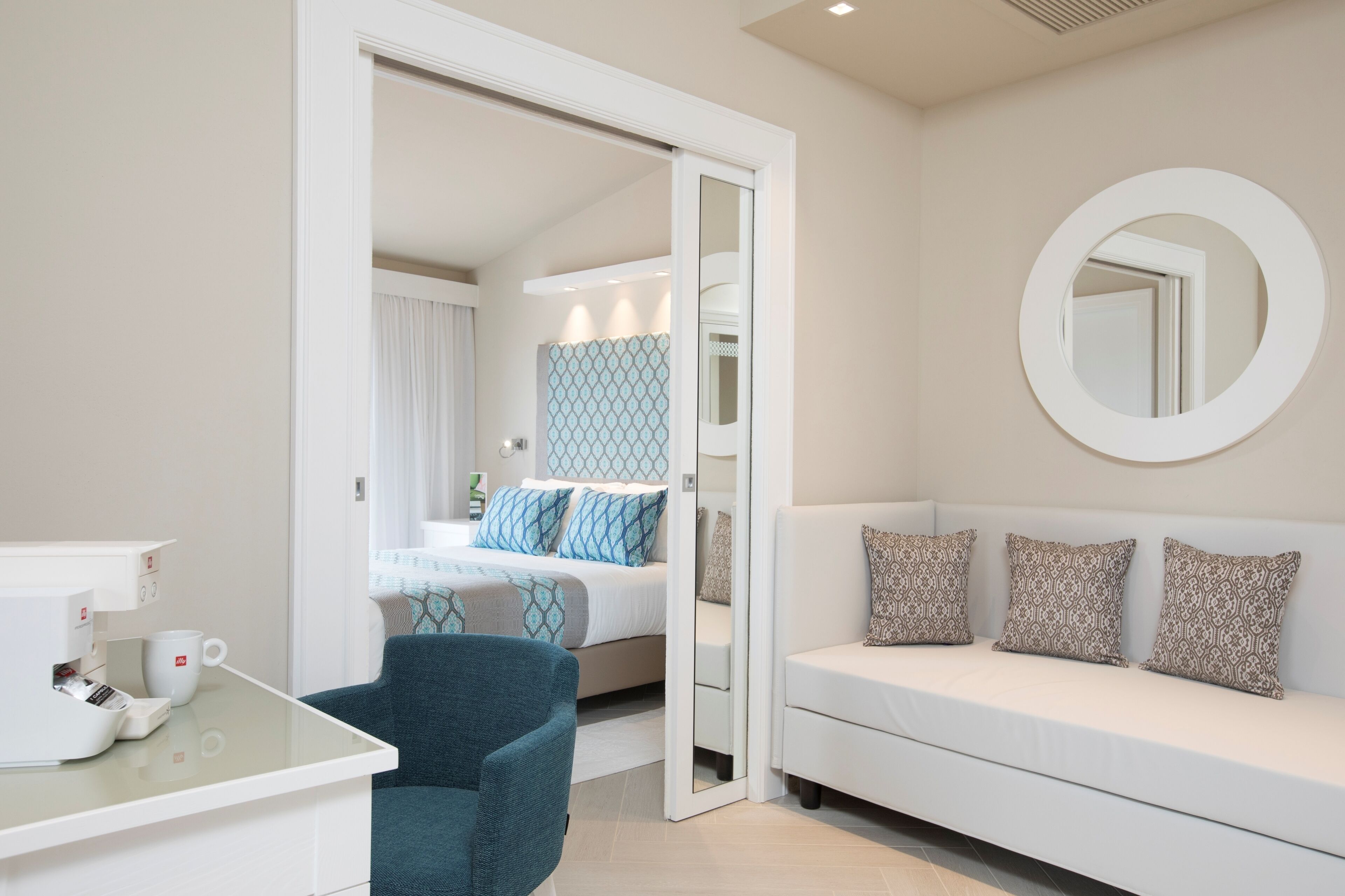 Een hotelkamer met een bed, een witte bank, een koffieapparaat en een spiegel aan de muur.
