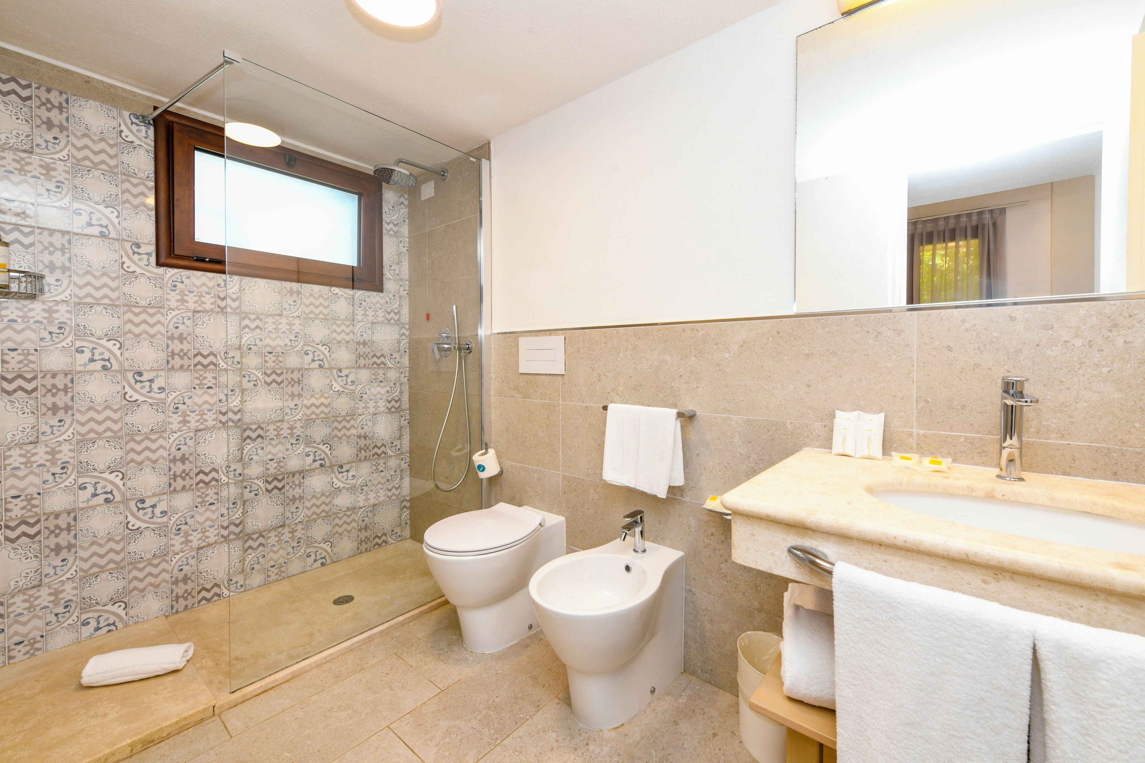 A bathroom with a shower, toilet, bidet, and a sink with a mirror.