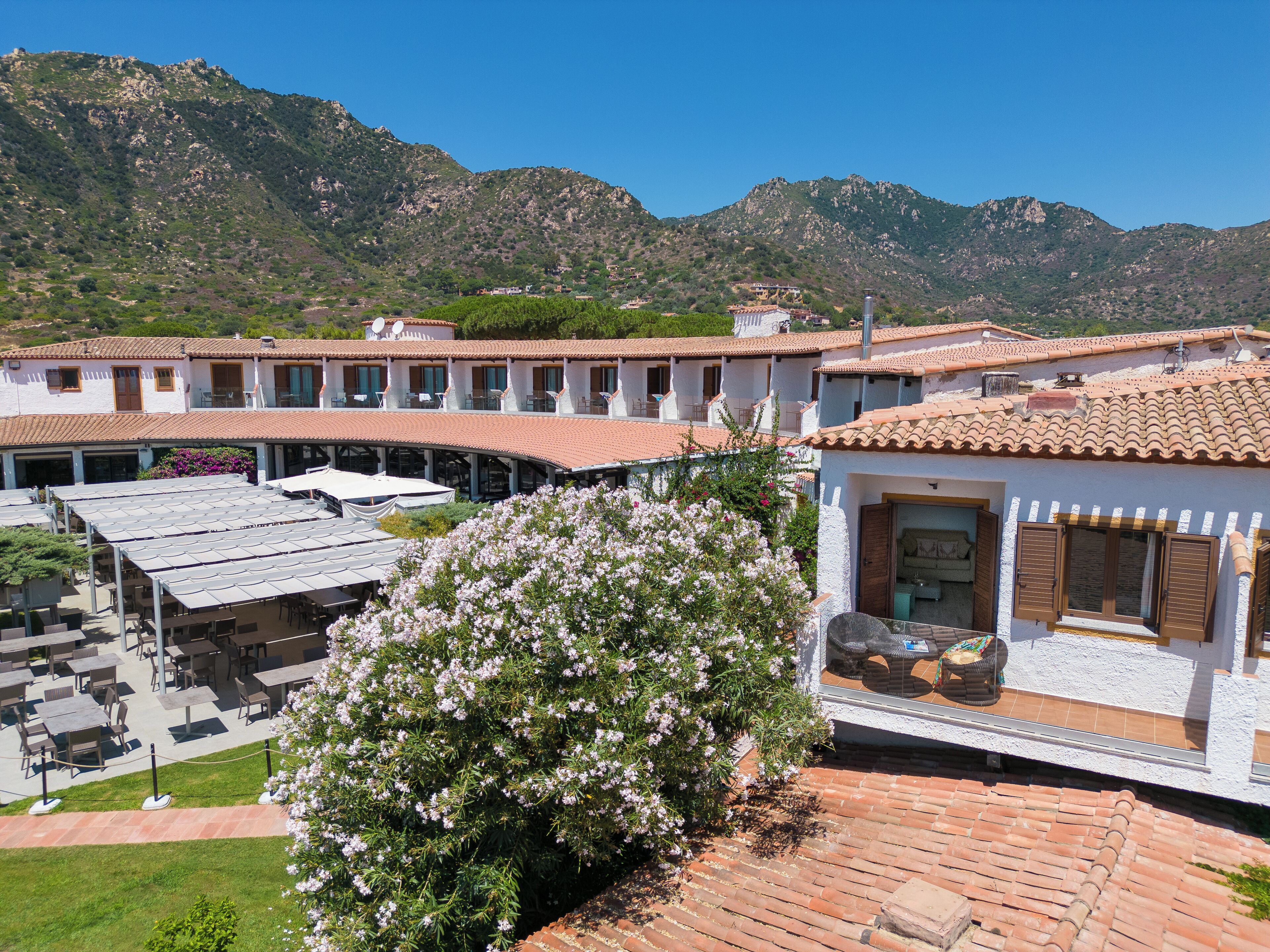 A courtyard with outdoor seating, a white building with a red-tiled roof, and a mountain backdrop.