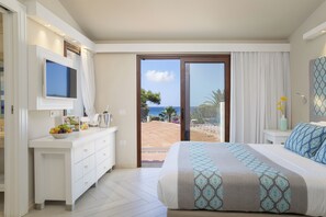 Un dormitorio con una cama grande, un televisor montado en la pared, un escritorio con un frutero y vista a la playa y al océano a través de una puerta corrediza de vidrio.