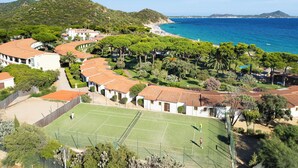 A coastal residential area with a tennis court, houses with red-tiled roofs, and a beach in the background. - Cormoran Resort Villasimius (Villasimius)