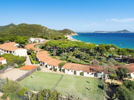 Zona residencial costera con cancha de tenis, casas con techo de tejas rojas y una playa al fondo.