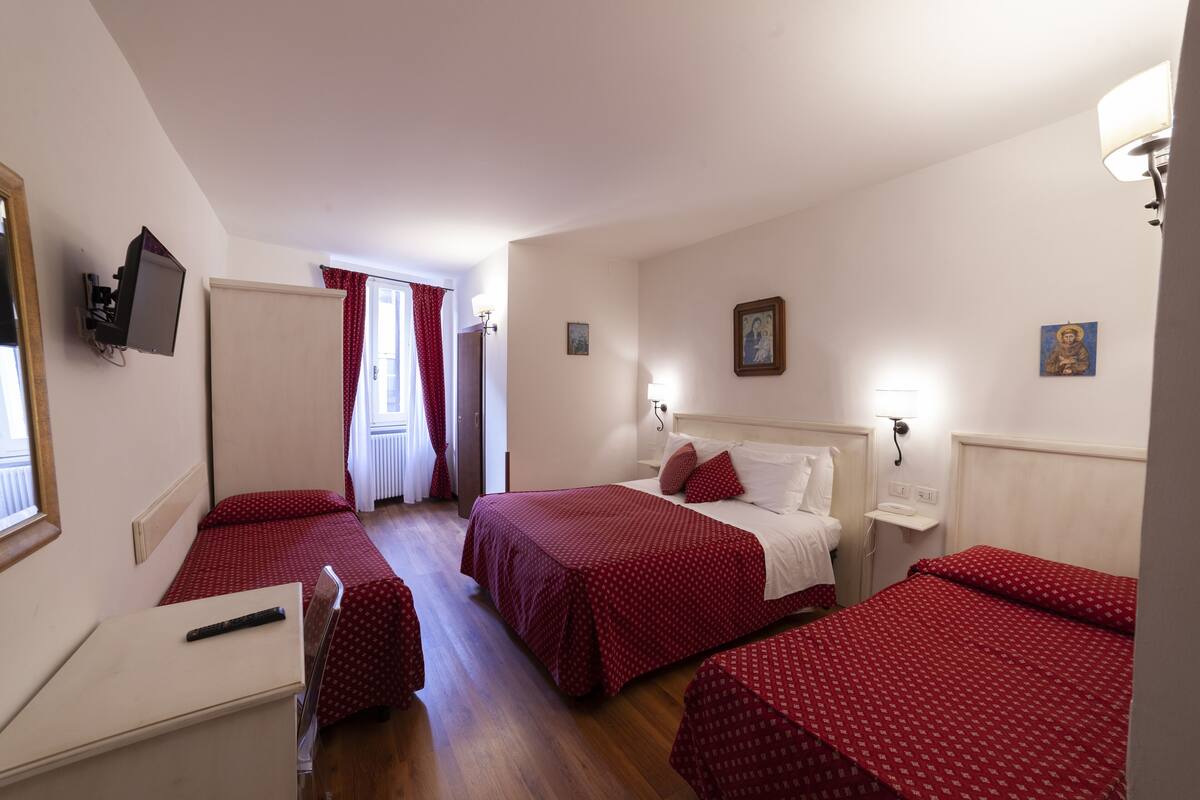 Quarto de hotel com duas camas, uma escrivaninha, uma cadeira, uma televisão e uma janela com cortinas.