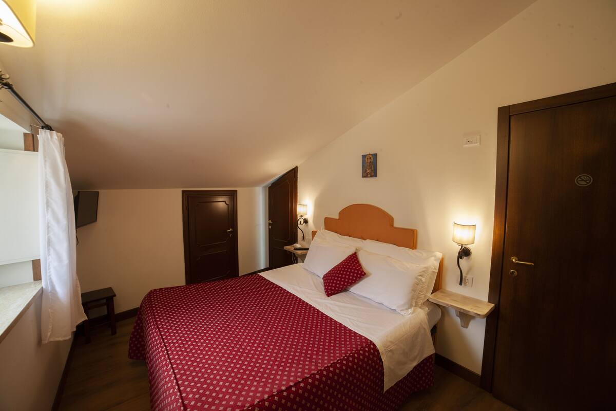 Quarto com cama, mesa de cabeceira, luminária na parede e porta.