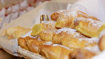 A basket of pastries, including croissants and a lemon tart, on a table.