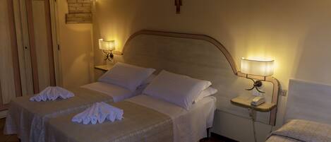 Habitación de hotel con dos camas, una pared de ladrillo, una cruz en la pared y lámparas de noche.