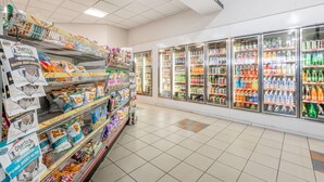 Un pasillo de supermercado con estantes llenos de aperitivos y una sección refrigerada con diversas bebidas.