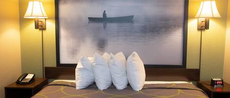 A hotel room with a bed, a nightstand with a phone, two wall-mounted lamps, and a large framed picture of a misty lake scene.