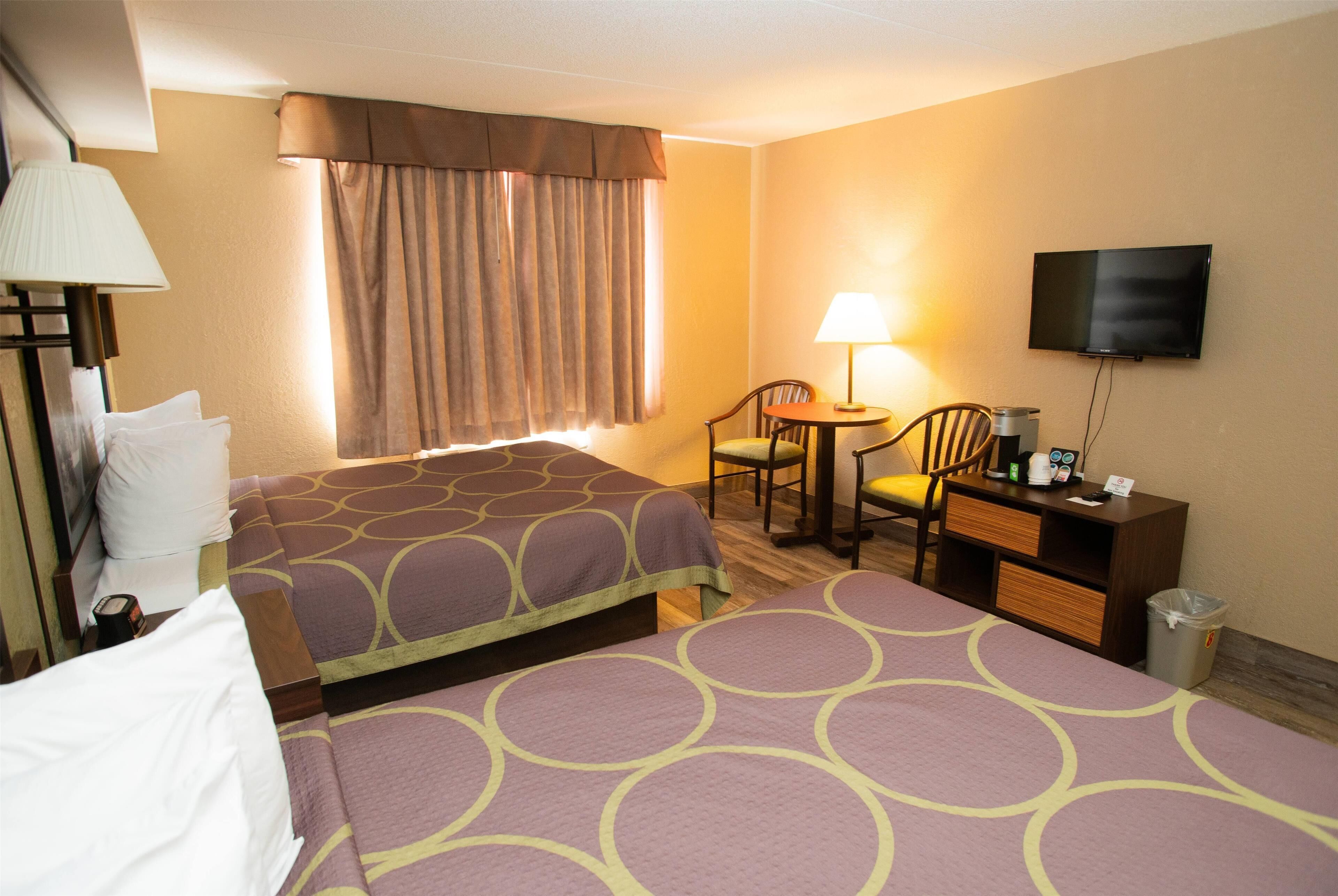 A hotel room with two beds, a desk, a chair, a TV, and a window with curtains.