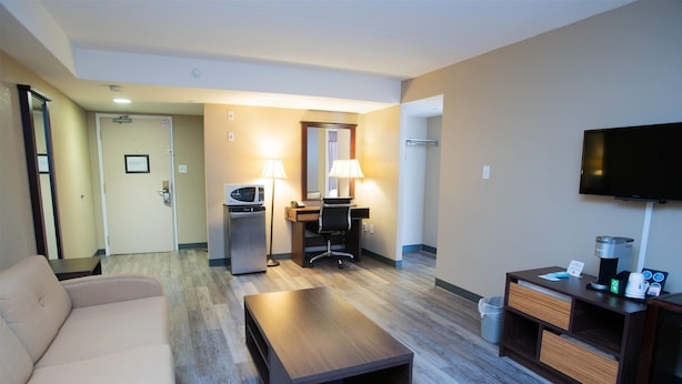 Habitación de hotel con sofá, una mesita de centro de madera, un escritorio con silla, televisor y minibar.