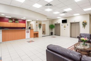 A reception area with a wooden counter, a waiting area with leather sofas, a potted plant, and a television mounted on the wall.