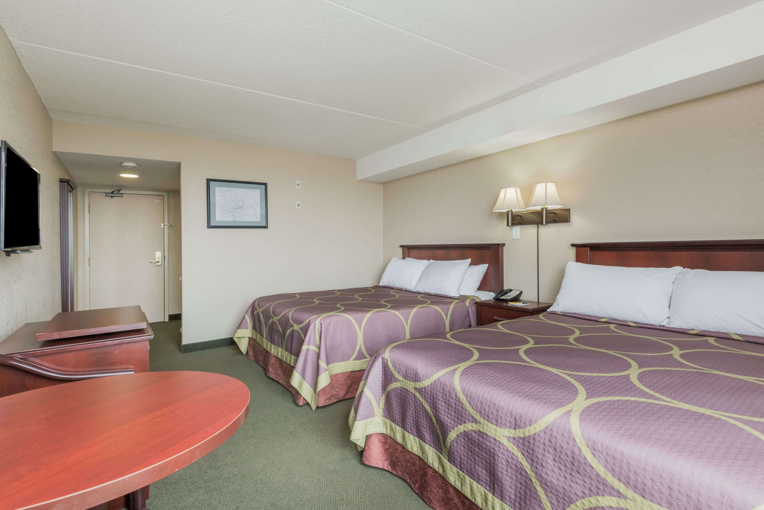 Habitación de hotel con dos camas, un escritorio, un televisor y un cuadro en la pared.