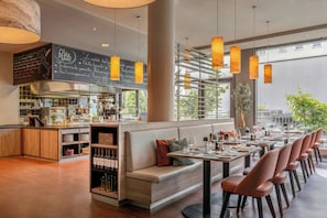 A modern restaurant interior with a long counter, seating area, and a chalkboard menu. - Courtyard by Marriott Munich City Center (Munich)