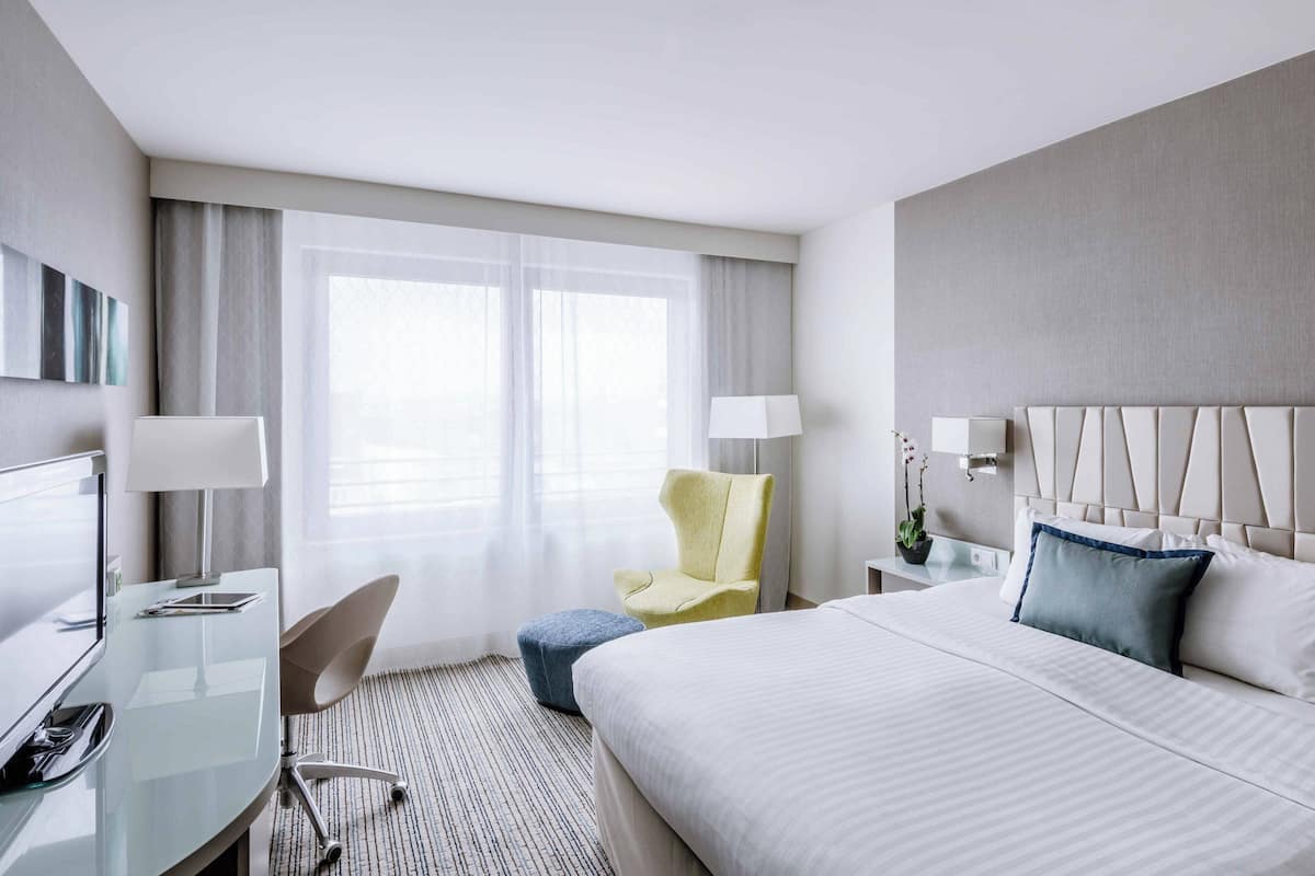 Une chambre d’hôtel avec un lit, un bureau avec un ordinateur, une chaise et une fenêtre avec des rideaux.