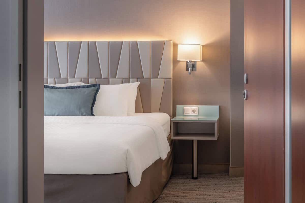 Une chambre d’hôtel avec un lit, une table de chevet, une lampe et un luminaire fixé au mur.
