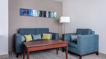 A hotel room with a blue sofa set, a wooden coffee table, a floor lamp, and a large abstract painting on the wall.