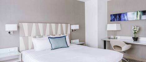A modern hotel room with a large bed, bedside tables, a desk, and a chair.