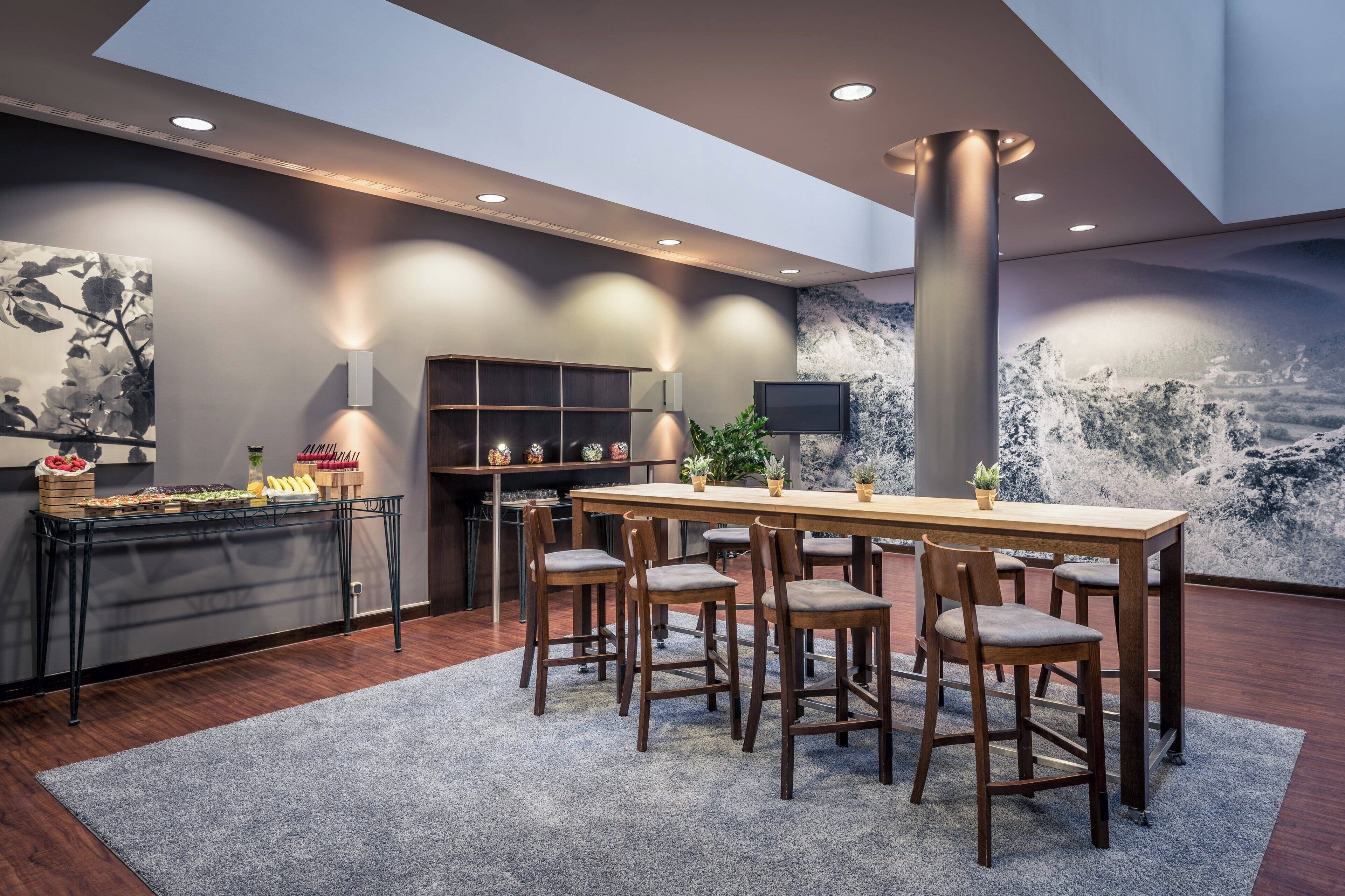 A modern dining area with a wooden table and chairs, a buffet with food and drinks, and a large wall mural.