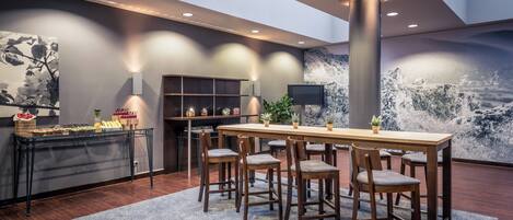 A modern dining area with a wooden table and chairs, a buffet with food and drinks, and a large wall mural.