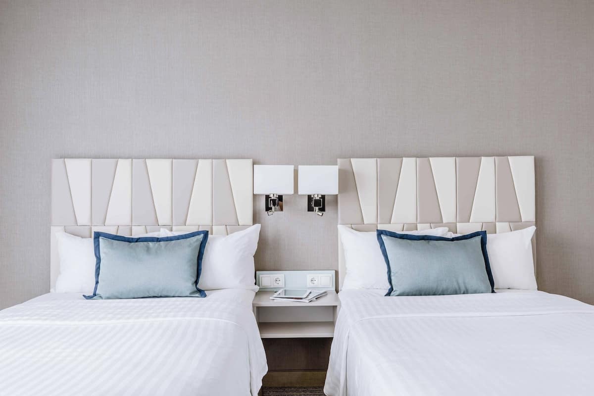 Une chambre d’hôtel avec deux lits, une table de chevet et une lampe fixée au mur.