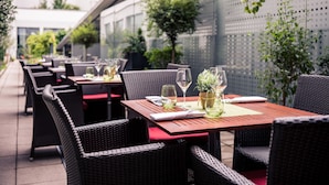 Un área de comedor al aire libre con sillas y mesas de mimbre, algunas con cojines rojos.