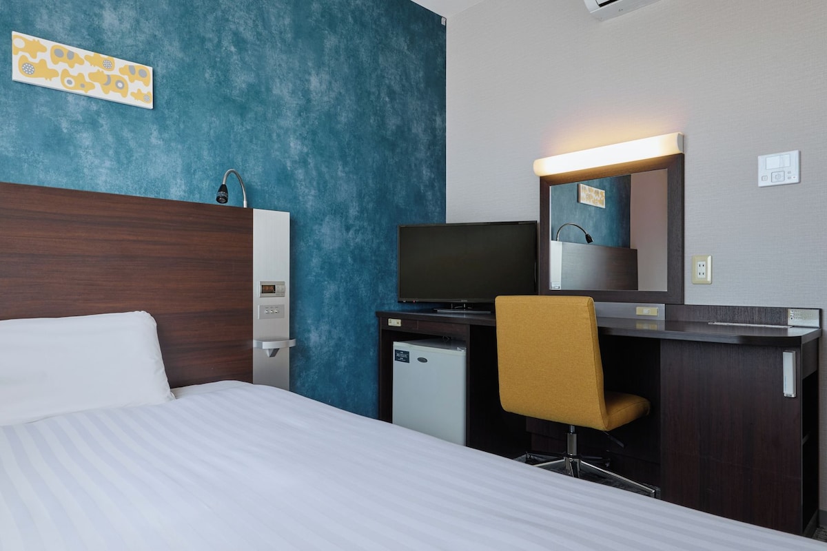 Une chambre d’hôtel équipée d’un lit, d’un bureau, d’une télévision et d’un petit réfrigérateur.