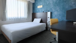 Una habitación de hotel con cama, escritorio, silla, televisor y panel de control en la pared.