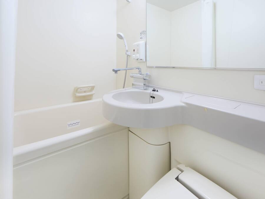 A white bathroom with a sink, a mirror, and a showerhead.