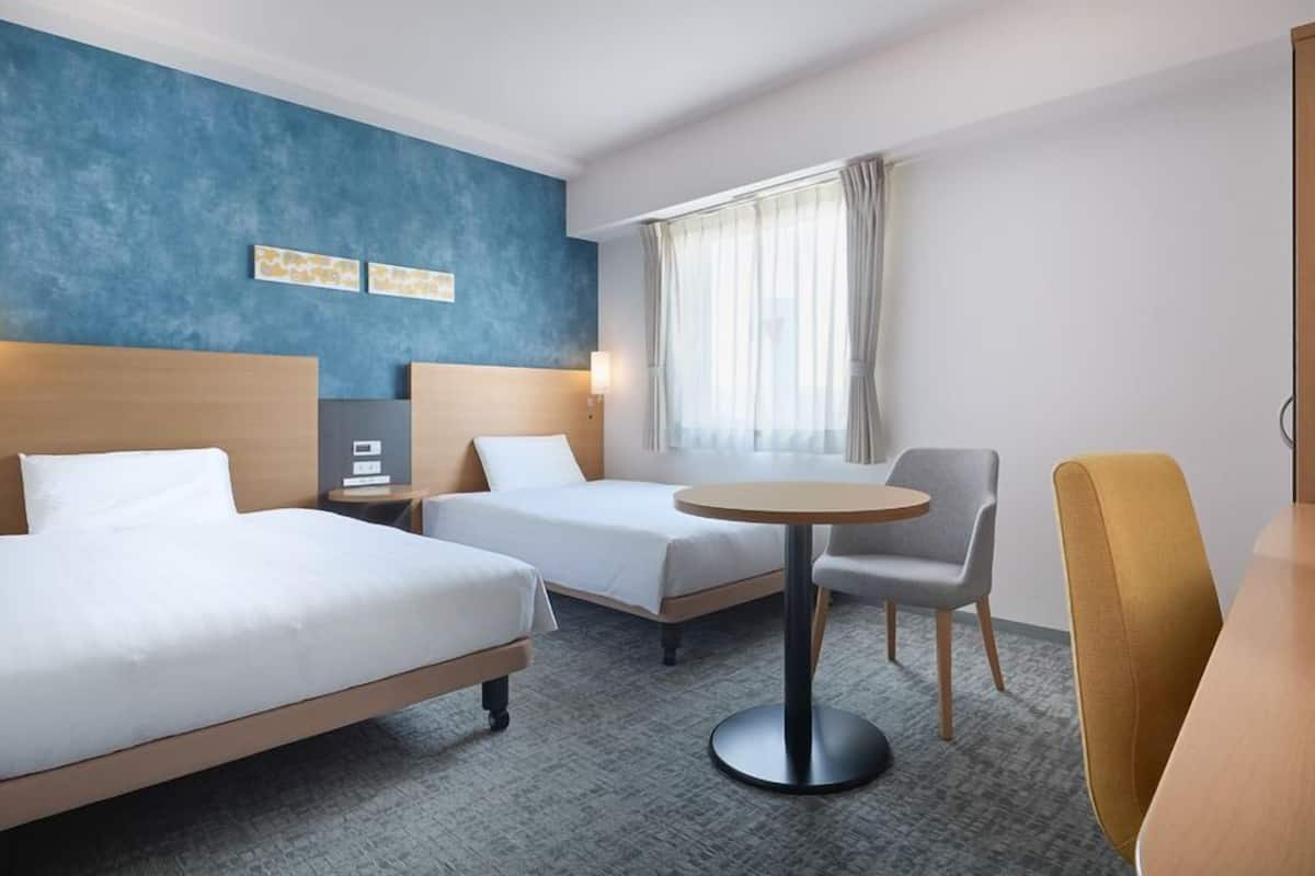 Une chambre d’hôtel avec deux lits, une petite table ronde, une télévision et une fenêtre avec des rideaux.