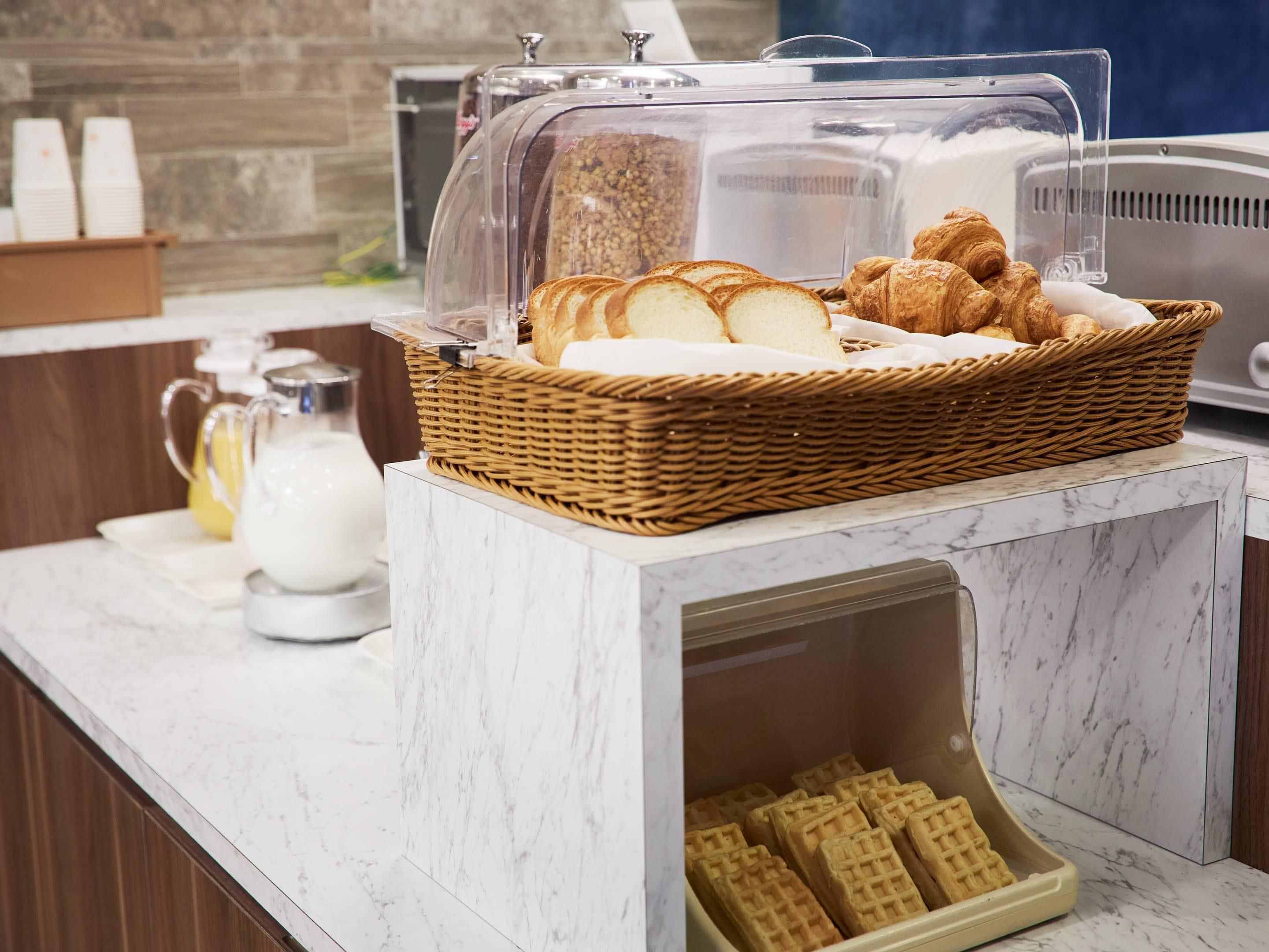 A breakfast buffet with bread, croissants, and waffles.