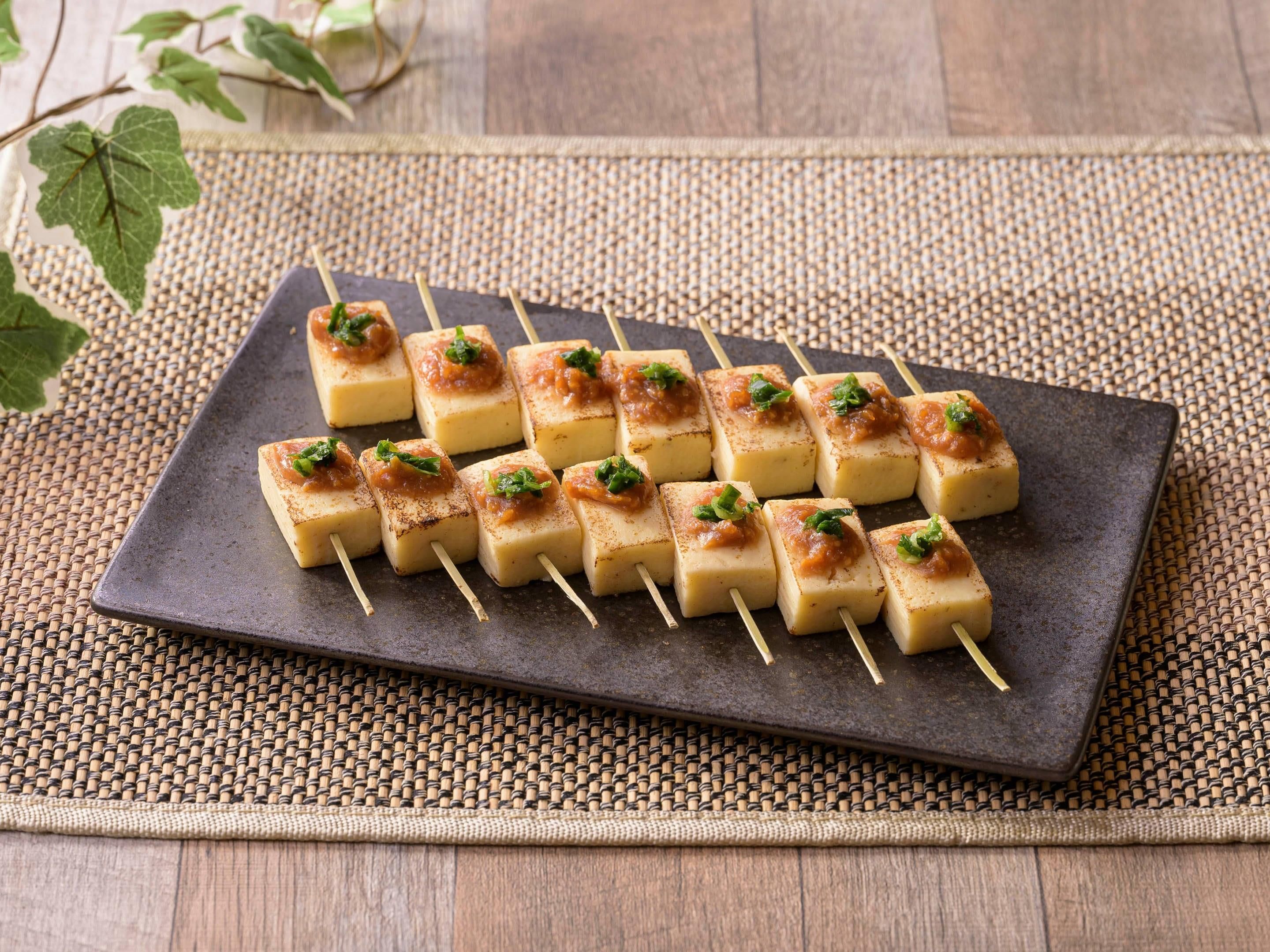 A rectangular plate with skewered food items, placed on a woven mat.