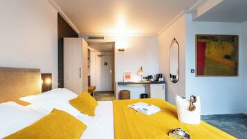 Une chambre d’hôtel avec deux lits, un bureau, une chaise, une machine à café et un tableau au mur.
