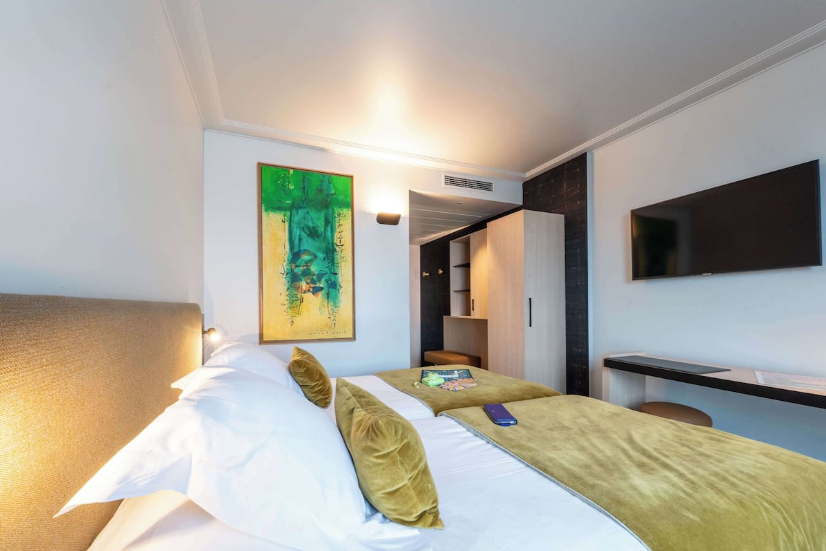 Habitación de hotel con cama, escritorio, silla, televisor y un cuadro en la pared.