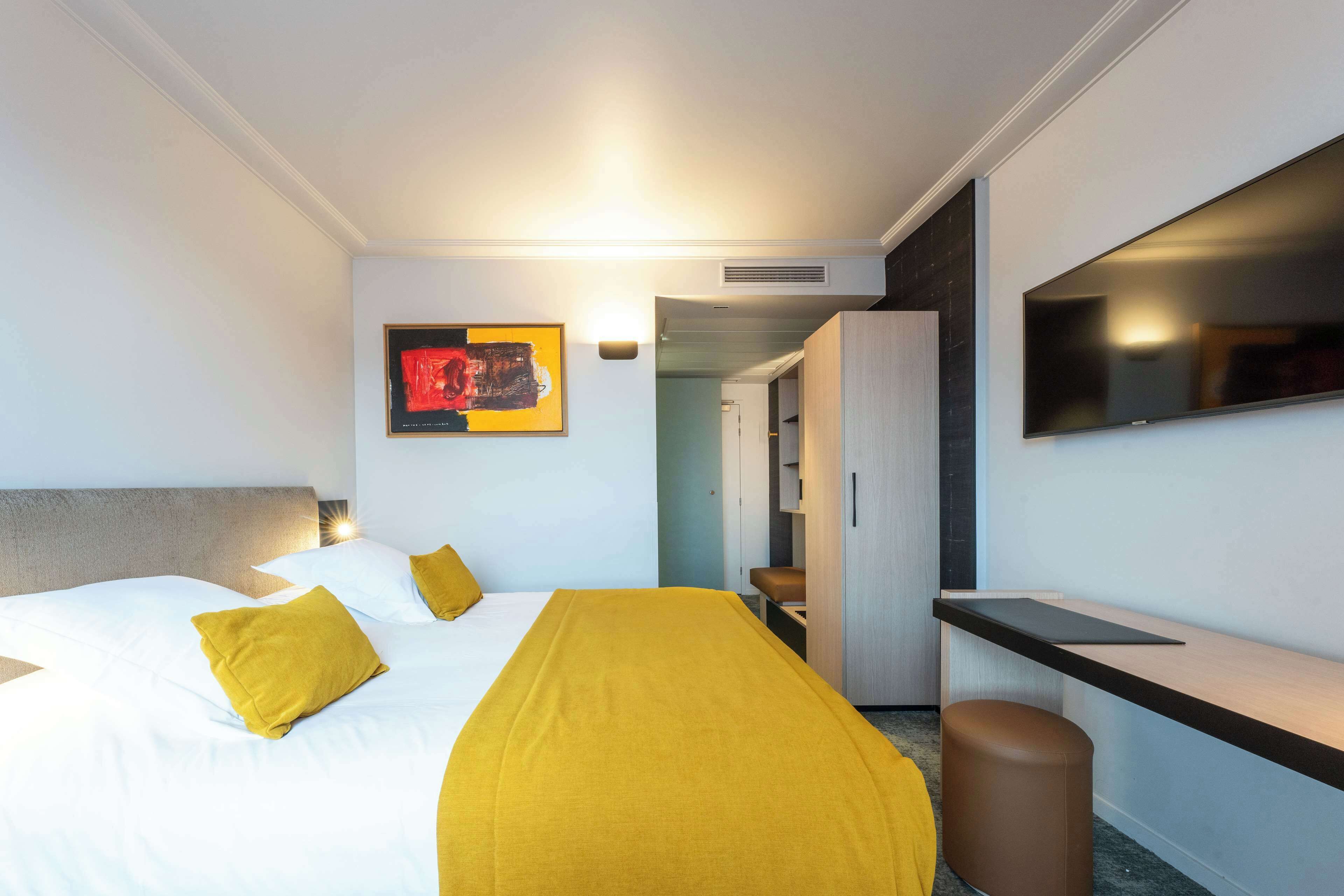 A hotel room with a bed, a desk, a chair, a TV, and a wardrobe.