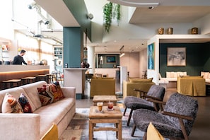 A modern interior with a bar area, seating, and a kitchen in the background. - Best Western Premier Le Masq Hotel (La Rochelle)