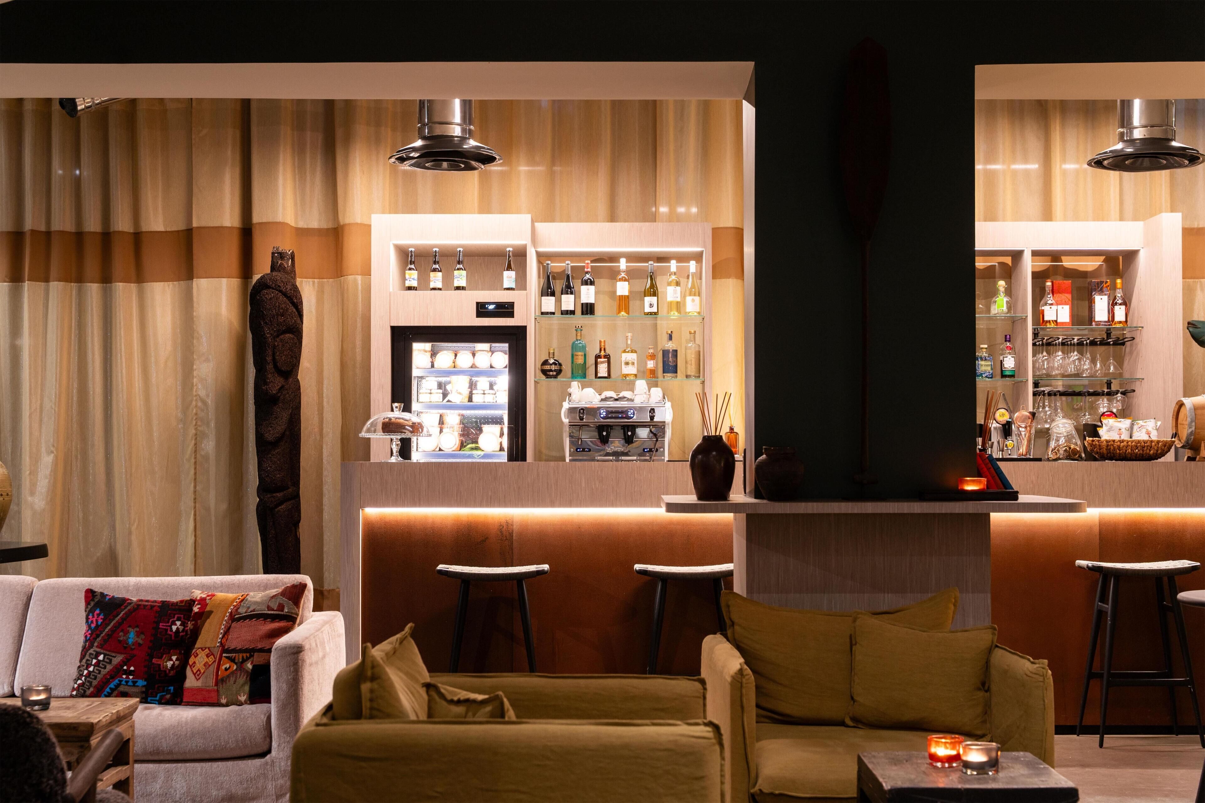 A bar area with stools, a counter with bottles, and a seating area with sofas and a decorative wall.