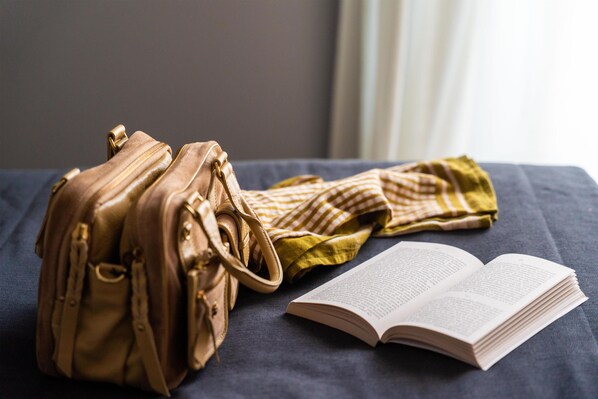 Un lit recouvert d’une couverture bleue, un sac à main beige, un tissu à rayures et un livre ouvert.