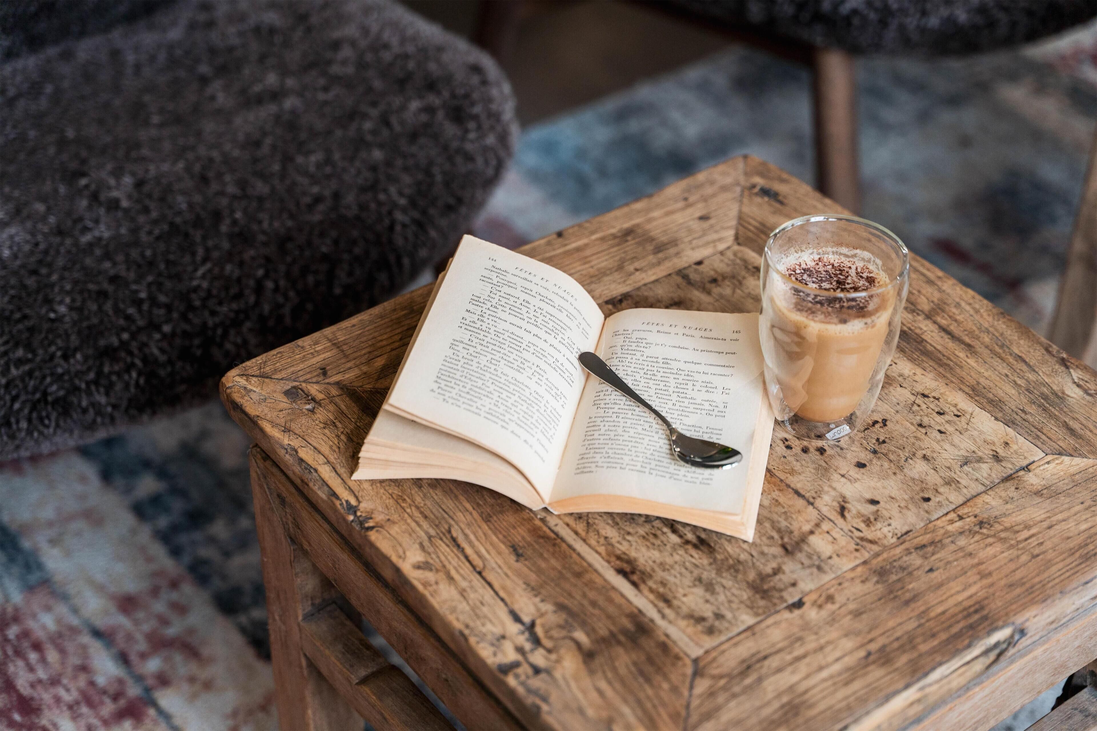Un libro abierto sobre una mesa de madera, con una cuchara y un vaso de una bebida.