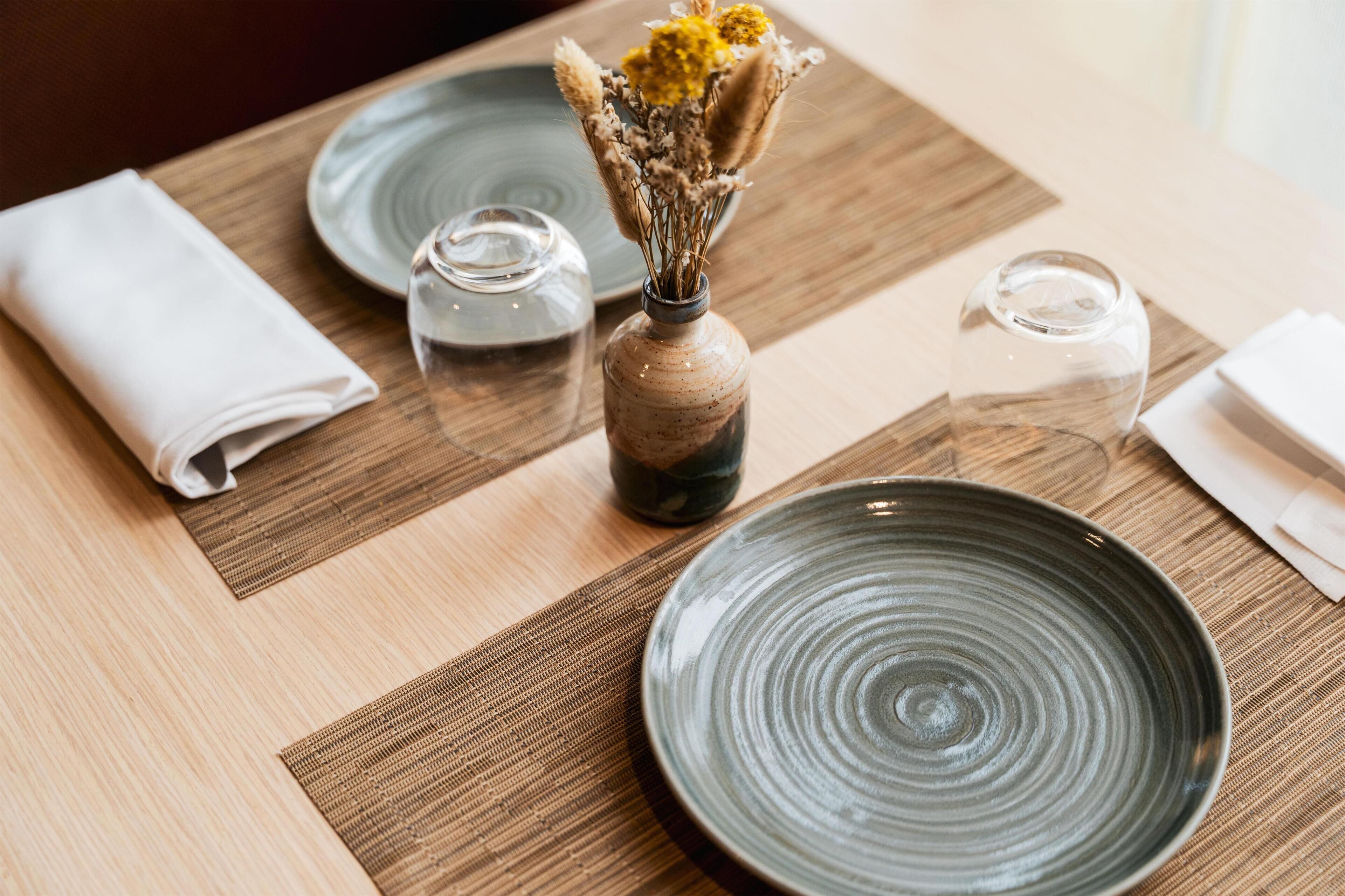 A dining table with a plate, a vase with dried flowers, and a folded napkin.