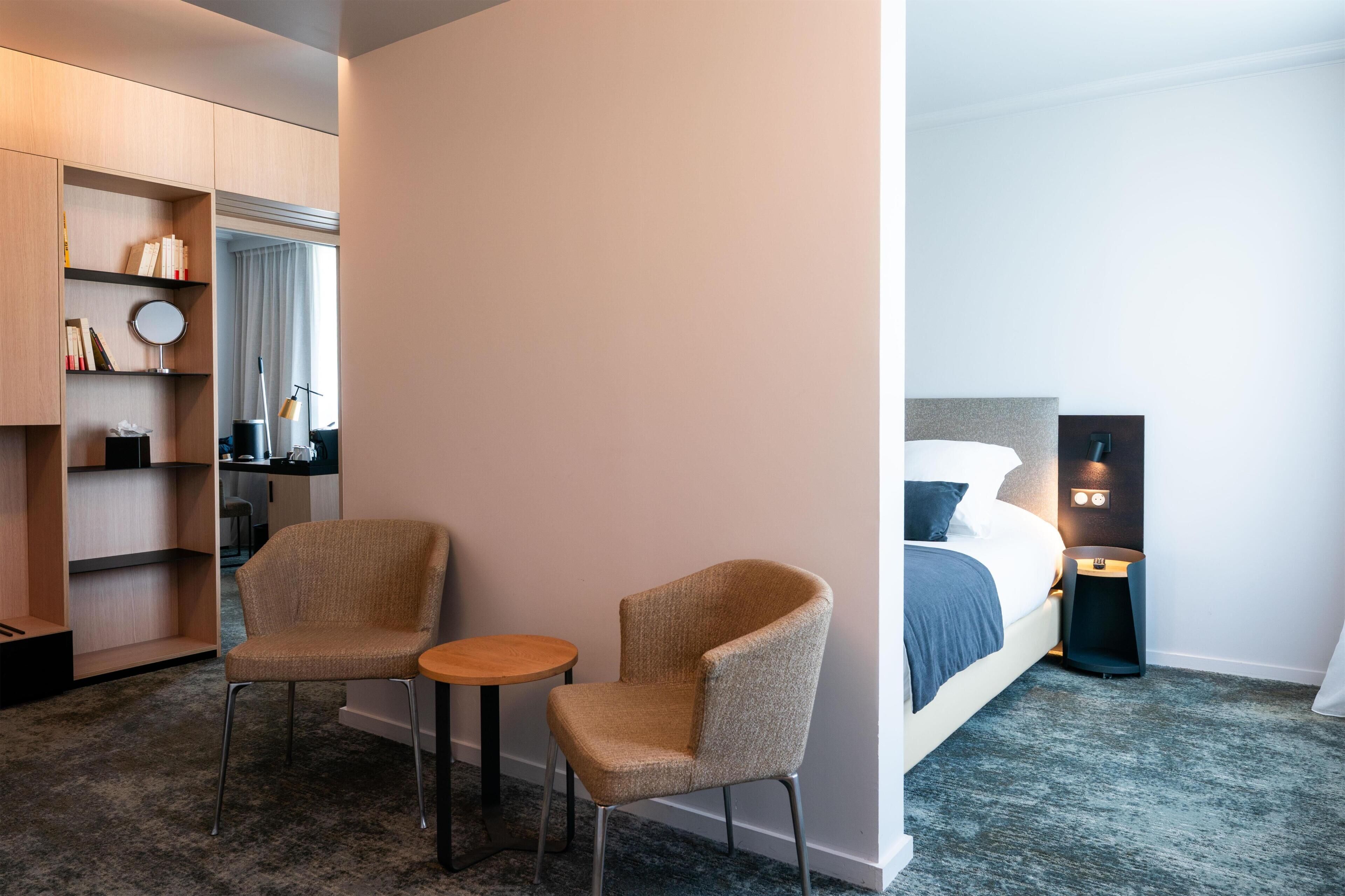A hotel room with a bed, a bedside table, a lamp, and a seating area with two chairs and a small table.