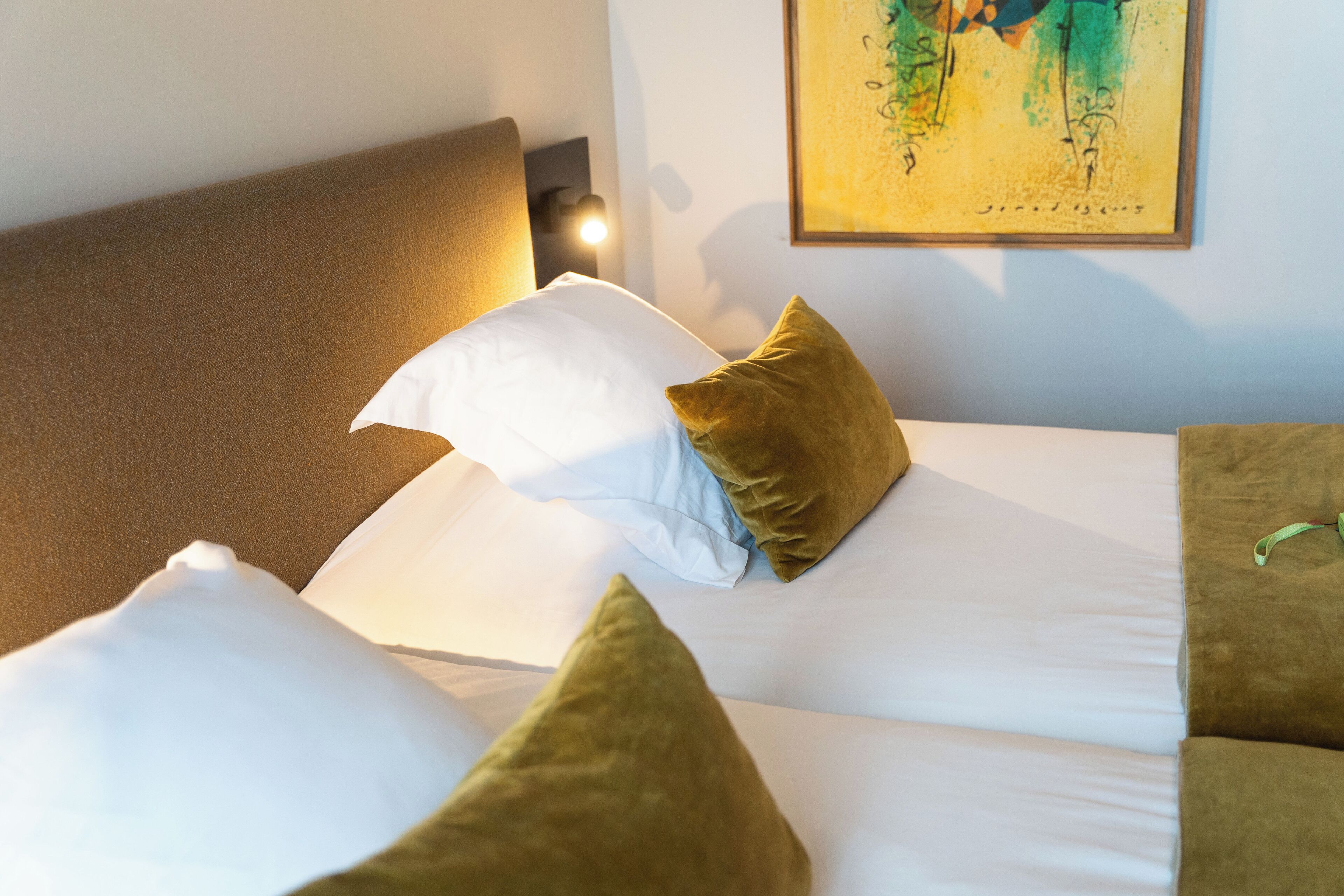 A neatly made bed with white sheets and two green pillows, a headboard, and a wall-mounted light.