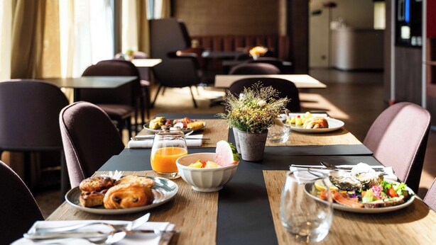 Un espace repas avec des tables préparées pour le petit-déjeuner, comprenant des croissants, des fruits et un bol de céréales.