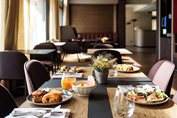 Un espace repas avec des tables préparées pour le petit-déjeuner, comprenant des croissants, des fruits et un bol de céréales.