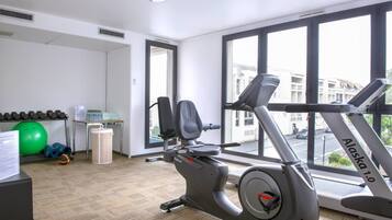 Une salle de sport équipée d’un tapis de course, d’un vélo d’exercice et de poids.
