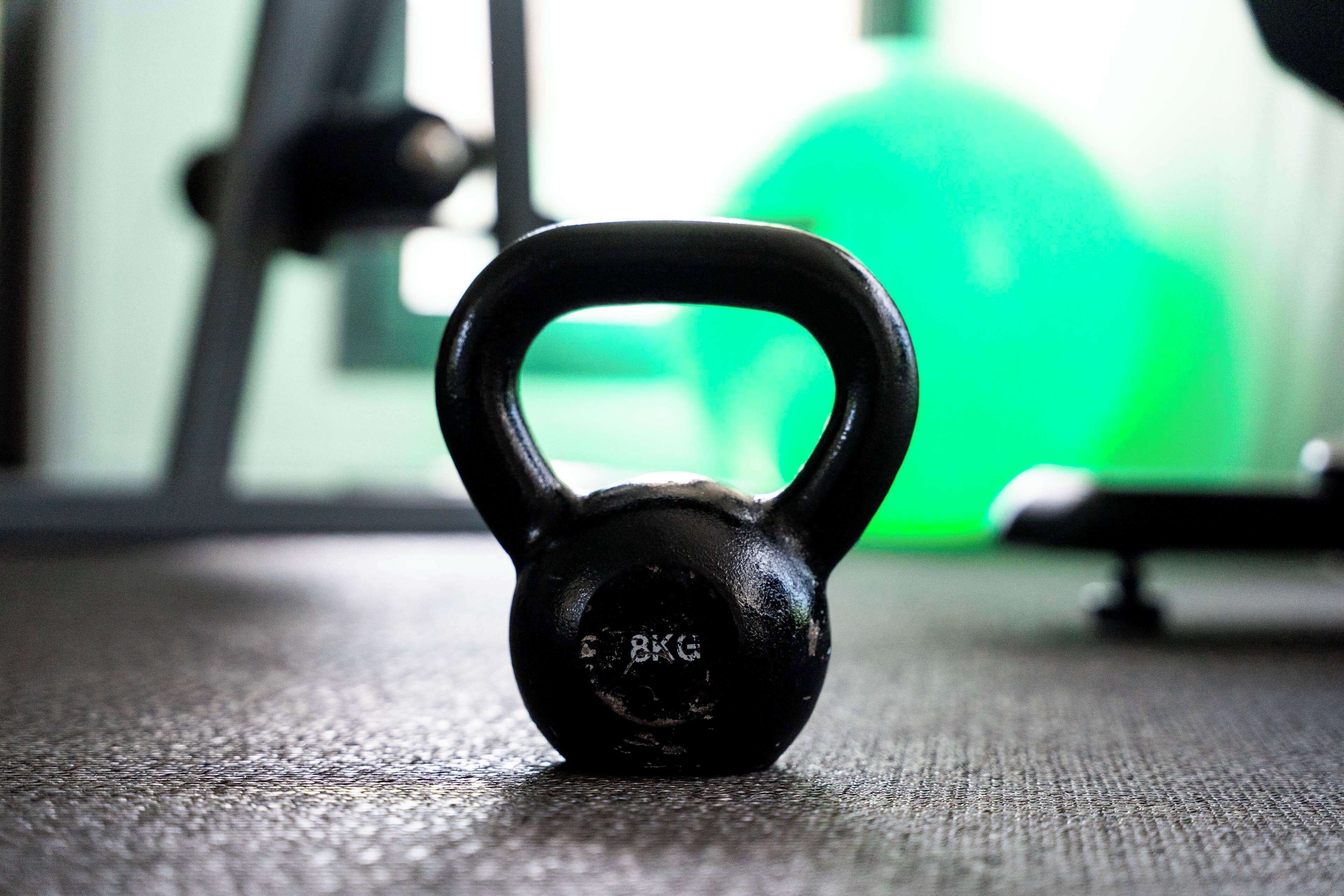 Una kettlebell negra sobre un suelo texturizado con un fondo verde desenfocado.