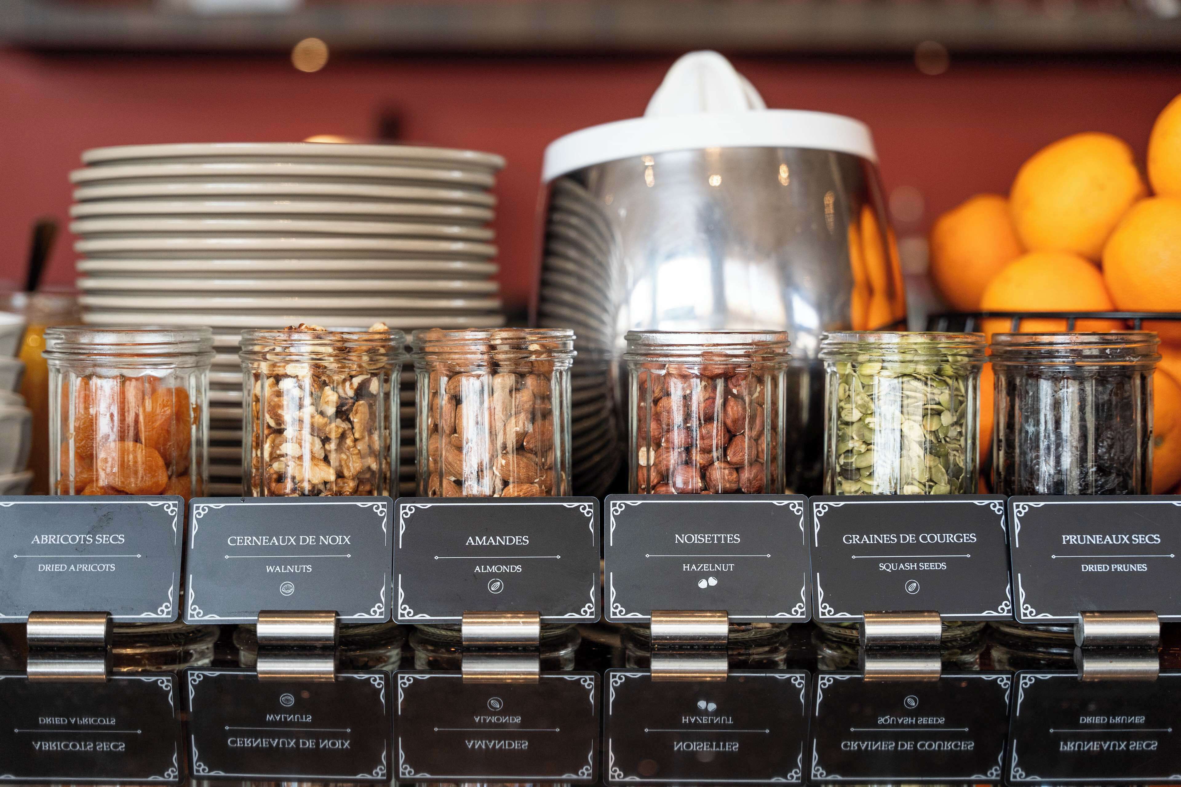 A display of various nuts and seeds in jars with labels, alongside plates and a large pot, likely in a kitchen or food preparation area.