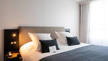 A hotel room with a large bed, two bedside tables, a nightstand, and a wall-mounted light fixture.