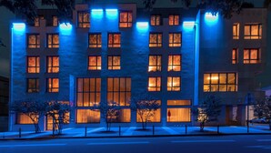 Un bâtiment moderne doté de nombreuses fenêtres et d’une façade plate, illuminé par un éclairage intérieur bleu et chaleureux.